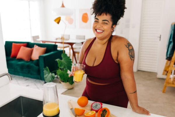 happy woman holding a glass of fresh juice in the kitchen while chopping up fruits for her weight loss goals