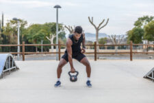 a handsome gentleman lifting a heavy kettlebell during his training in a city park on a nice day