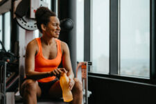 Beautiful fitness woman dressed up in sportswear sitting at gym resting after workout and thoughtfully looking into the distance holding a water bottle