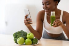 a young beautiful woman looking at her phone to read about losing stomach fat as she enjoys her smoothie