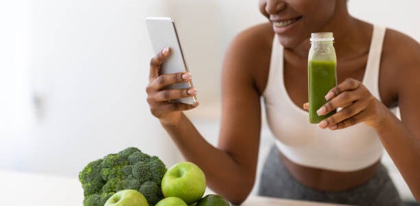 a young beautiful woman looking at her phone to read about losing stomach fat as she enjoys her smoothie