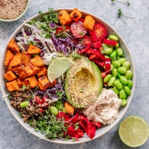 a colorful vegan bowl with quinoa, sweet potato, avocado, hummus and variety of veggies