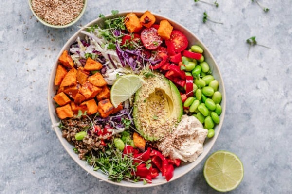 a colorful vegan bowl with quinoa, sweet potato, avocado, hummus and variety of veggies